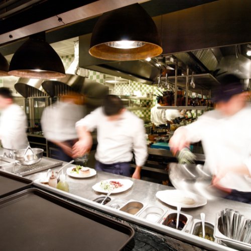 Line of chefs and cooks in a kitchen, blurred to show their motion.